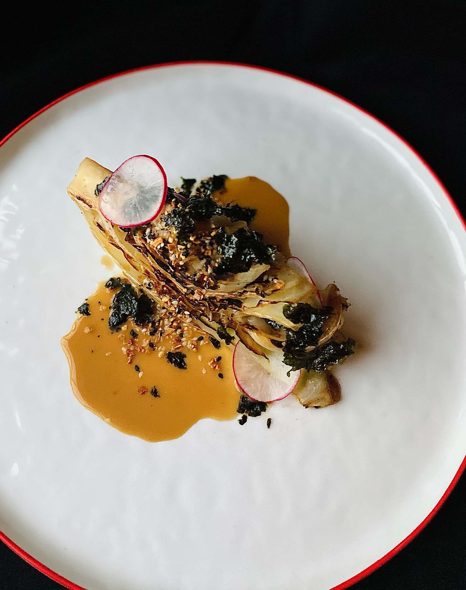 Charred cabbage with almond coconut yogurt sauce & seaweed furikake on a white plate with red trim