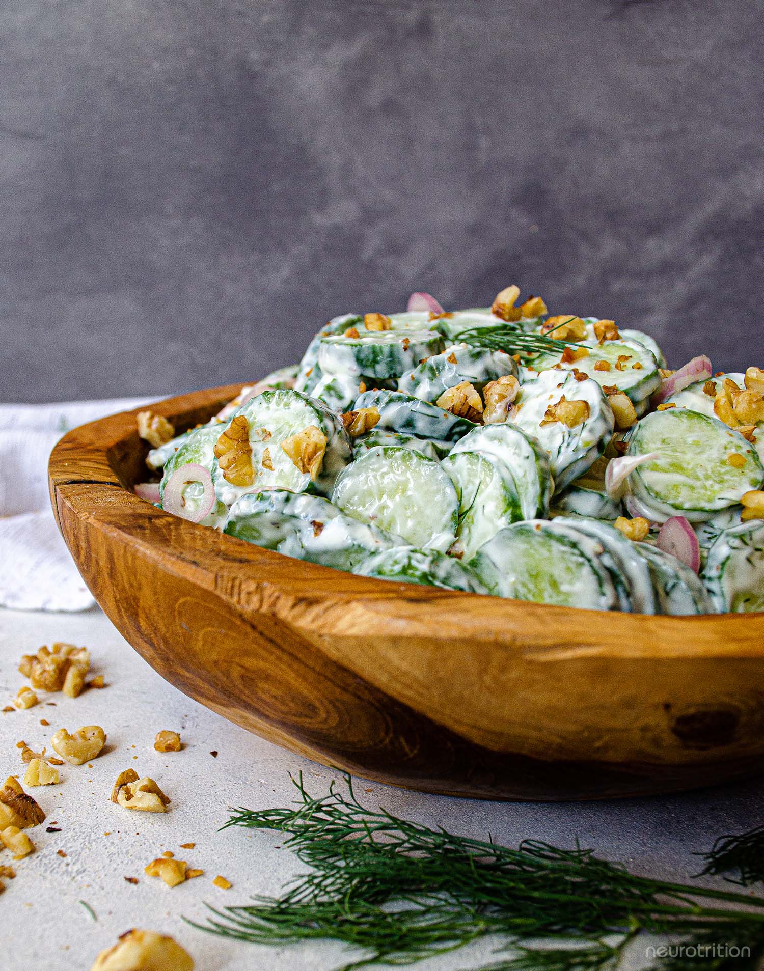 Sliced cucumbers and chopped walnuts in a creamy dressing inside a wooden bowl, topped with dill springs.