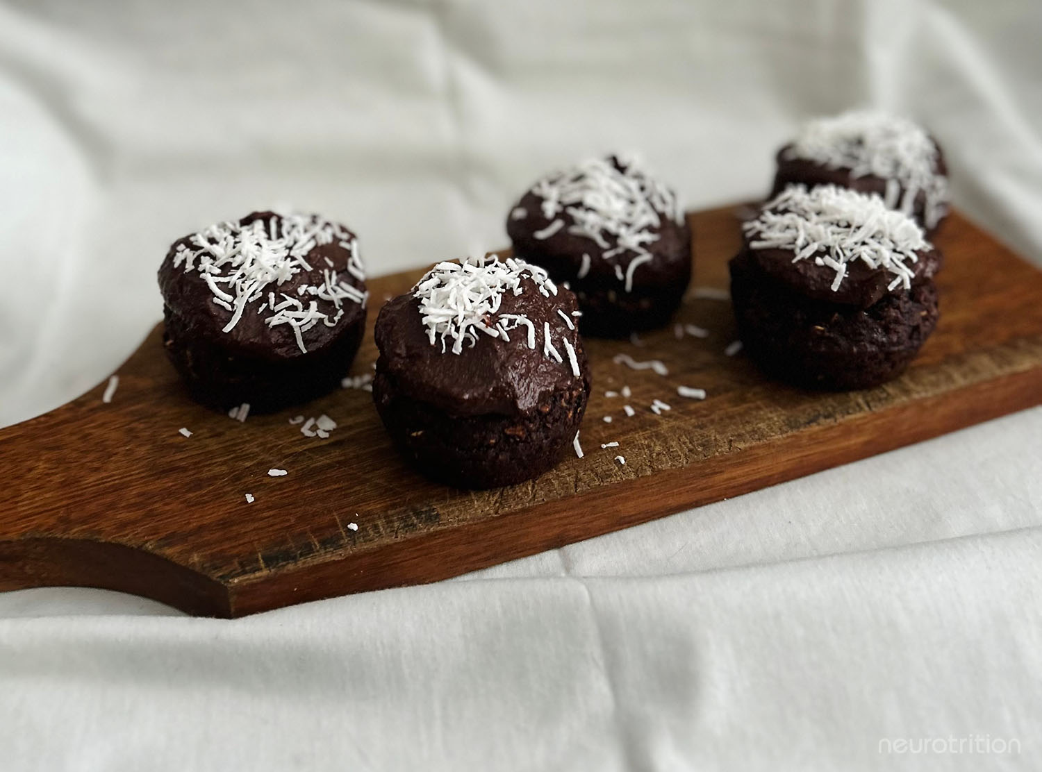 Fudgy chocolate cupcakes with sweet potato frosting topped with shredded coconut on wooden cutting board.