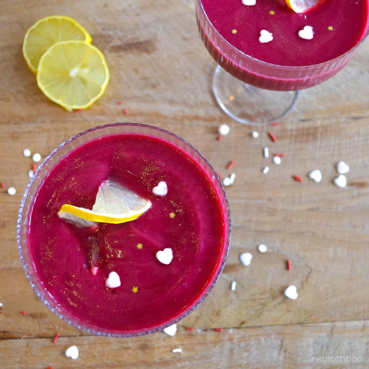 Two bright pink smoothies in cocktail glasses, with lemon twists and heart and star sprinkles.