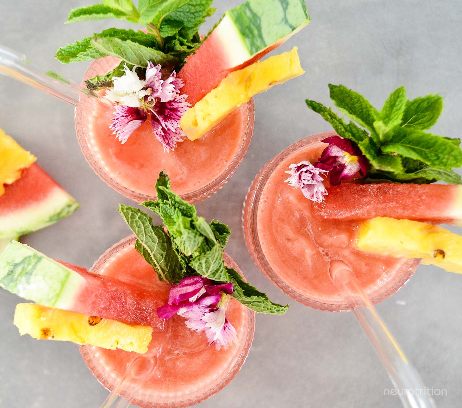 Top view of three watermelon pineapple coconut slushies, garnishes with fresh fruit and mint.