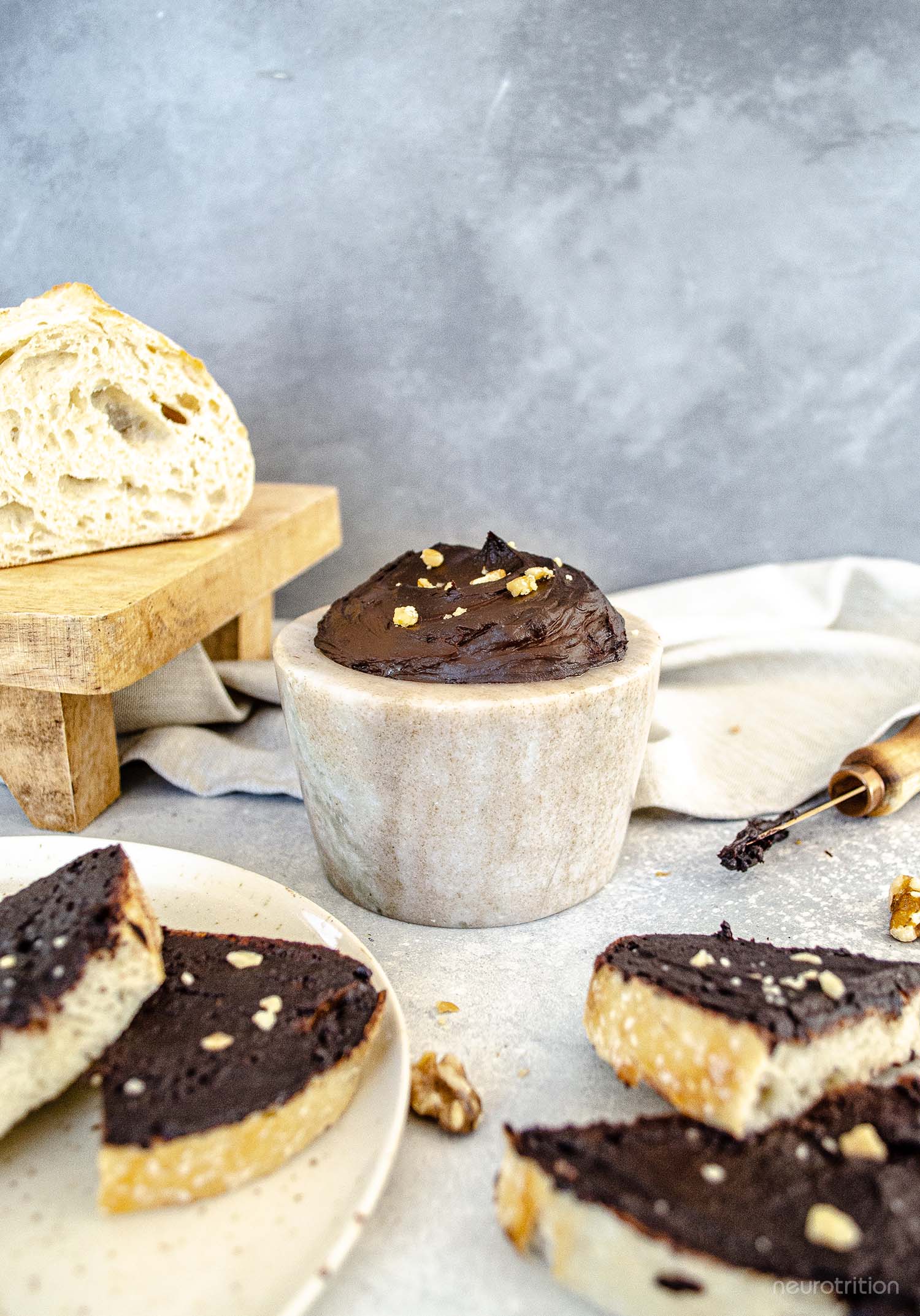 A stone dish full of homemade chocolate spread is surrounded by slices of bread that are covered in the chocolate spread and topped with crushed walnuts.
