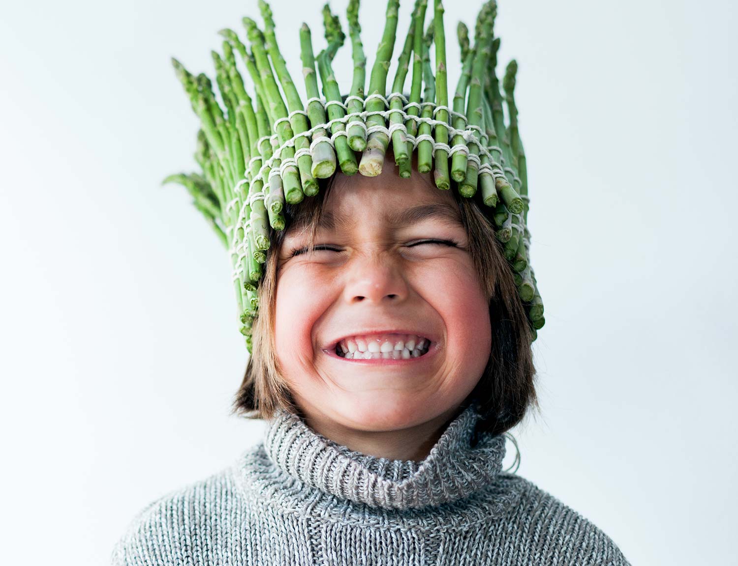 Young child wearing a crown made of asparagus