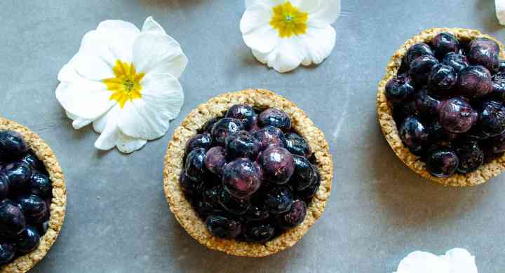 Looking down on six mini blueberry pies placed in a grid with little white and yellow flowers in between the pies.