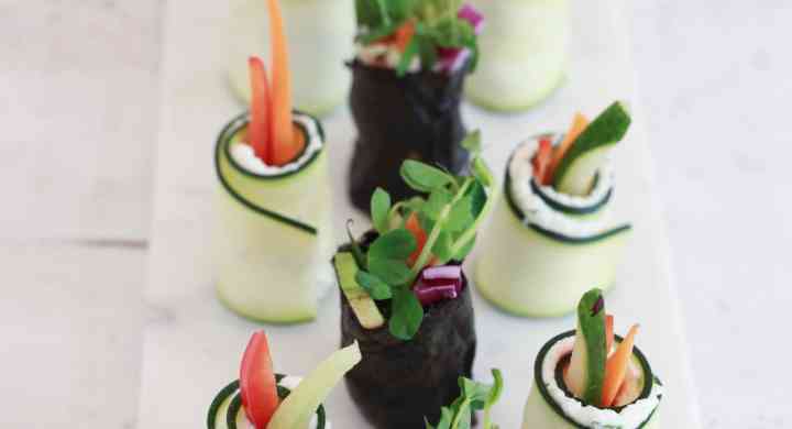 Veggie sushi wrapped in nori and raw zuchinni, on a white marble board.