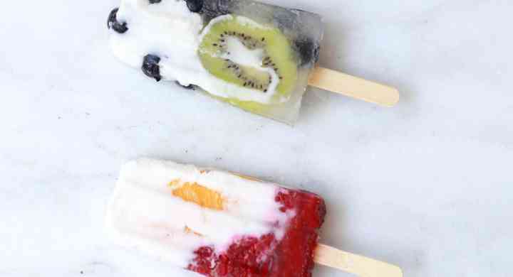 Four homemade popsicles in a row, with chunks of lime, blueberries, peaches and kiwi