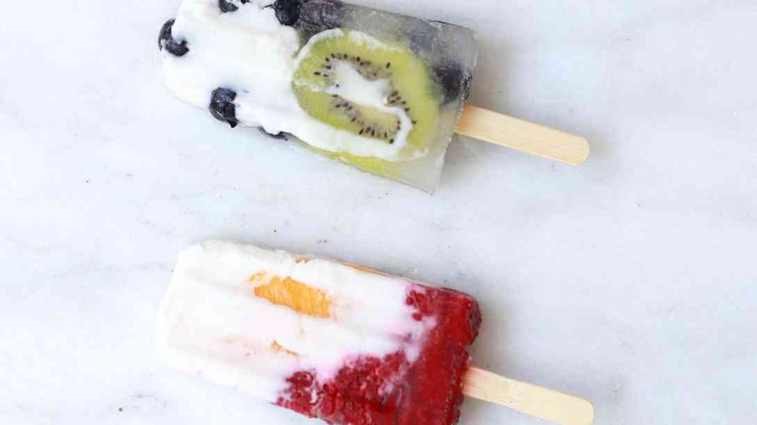 Four homemade popsicles in a row, with chunks of lime, blueberries, peaches and kiwi