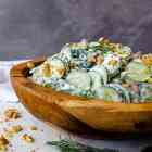 Sliced cucumbers and chopped walnuts in a creamy dressing inside a wooden bowl, topped with dill springs.