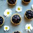 Looking down on six mini blueberry pies placed in a grid with little white and yellow flowers in between the pies.