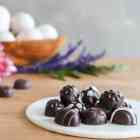 A pile of homemade chocolate Easter eggs with decorative white icing, on a white plate.